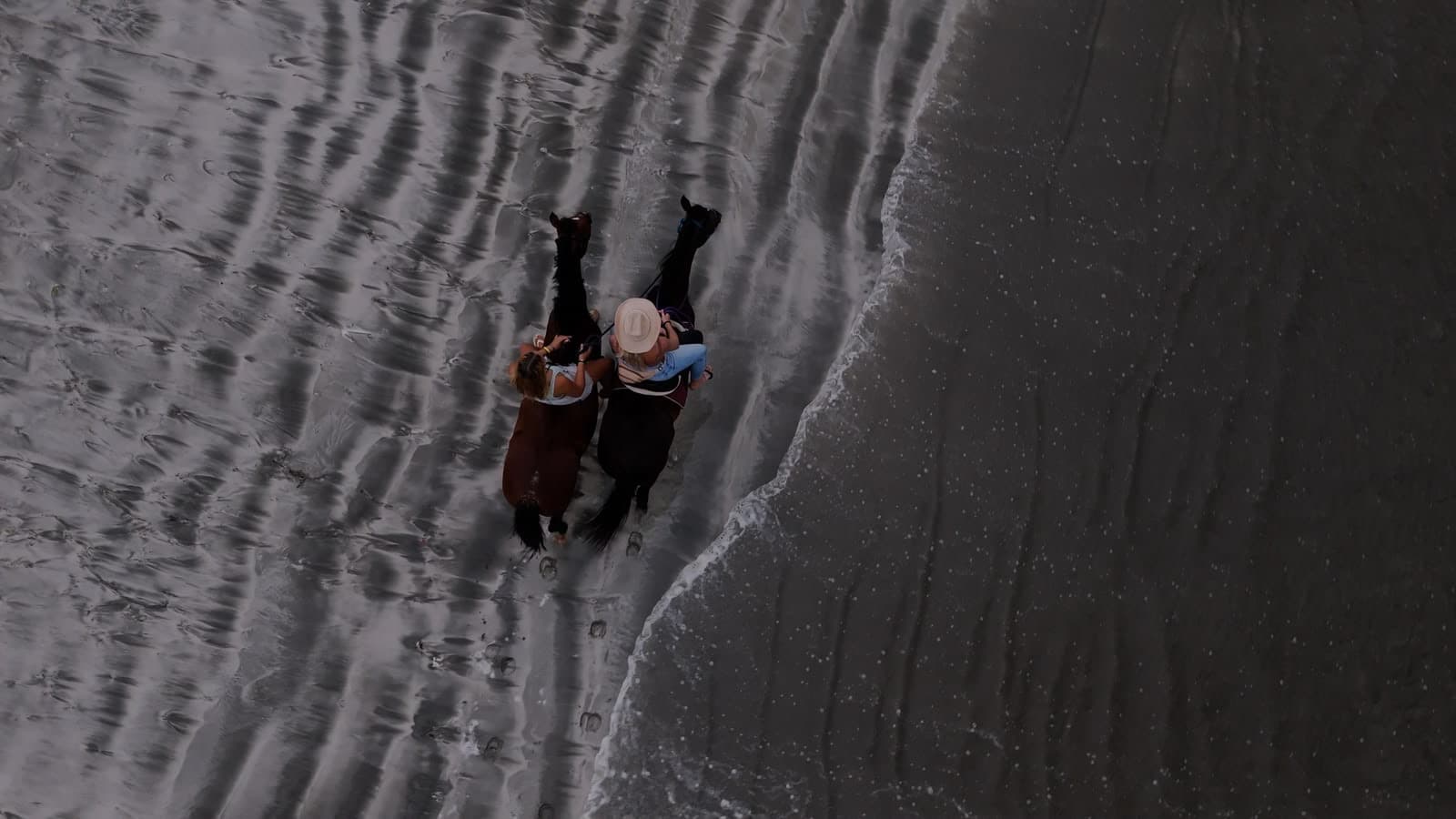 Aerial view of two horse riders at the water's edge on a beach in Bocas del Toro